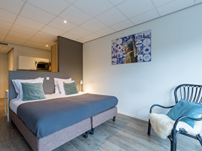 Een gezellige slaapkamer met een net opgemaakt bed, decoratieve kussens, een stoel en zachte verlichting. De kamer heeft warme wanden, elegant beddengoed en een houten nachtkastje.